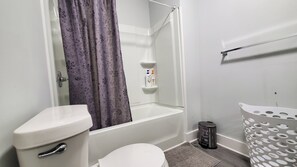 A bathroom with a toilet, a bathtub, and a shower. There are toiletries on the wall and a trash can. - 4 Beds 2 Bath House- 2 blocks to GWCC, Mercedes Benz Stadium, close to Downtown  (Atlanta)