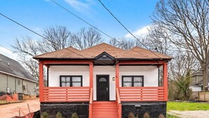 Ein zweistöckiges Haus mit rotem und weißem Anstrich, einer Veranda und einem schwarzen Dach.
