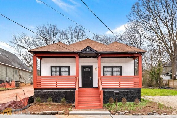Une maison à deux étages, avec une façade rouge et blanche, un porche à l’avant et un toit noir.