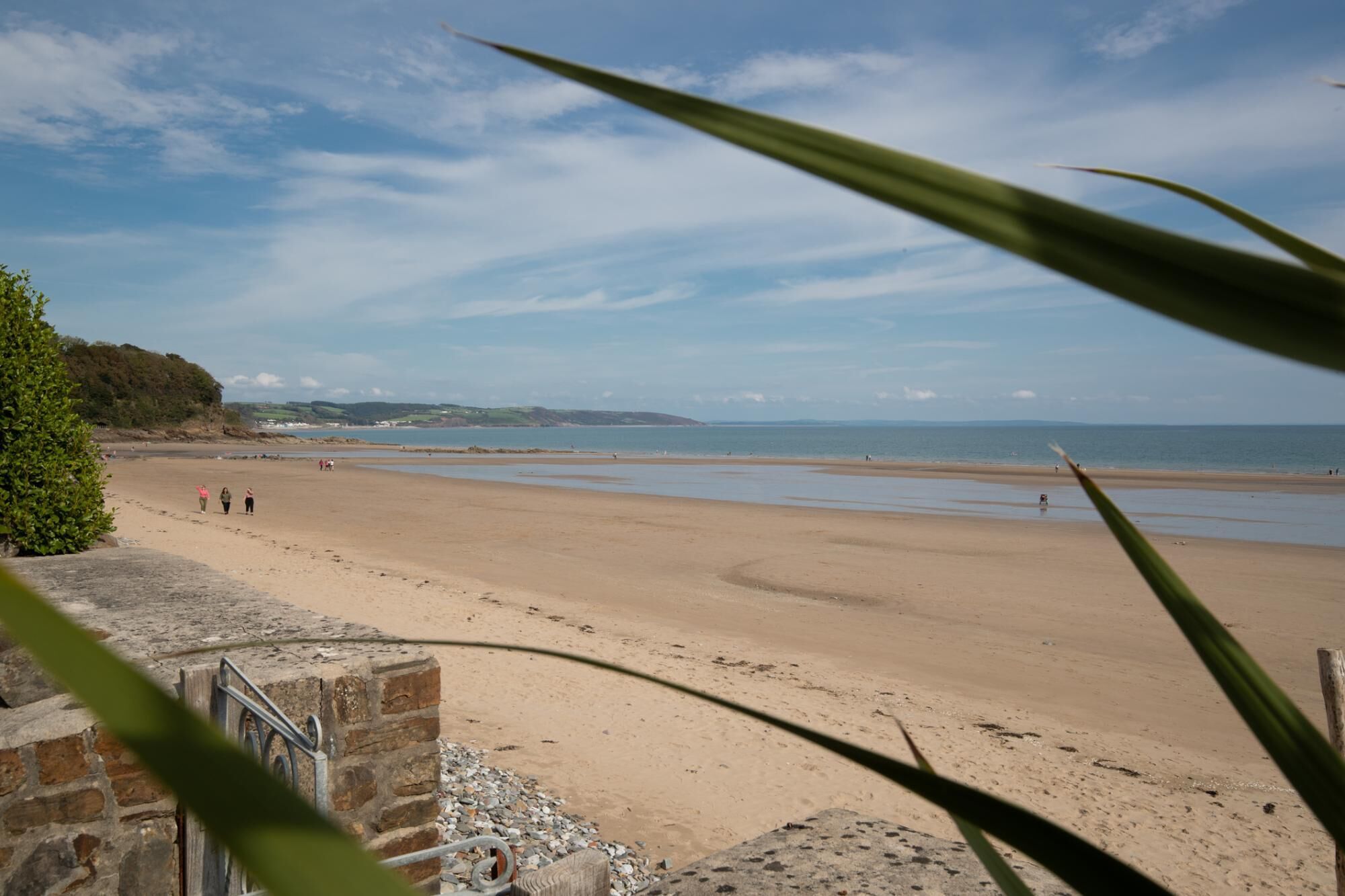 A beach with a stone wall and a metal railing in the foreground.