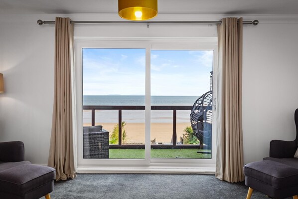 A room with a large sliding glass door leading to a balcony with a view of the beach.