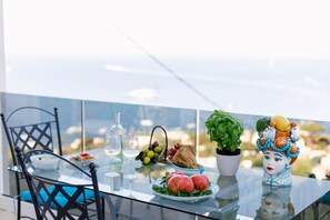 A glass table with a plate of fruit, a vase with green leaves, and a ceramic figure. - Casa Michela by Elite Villas (Capri)