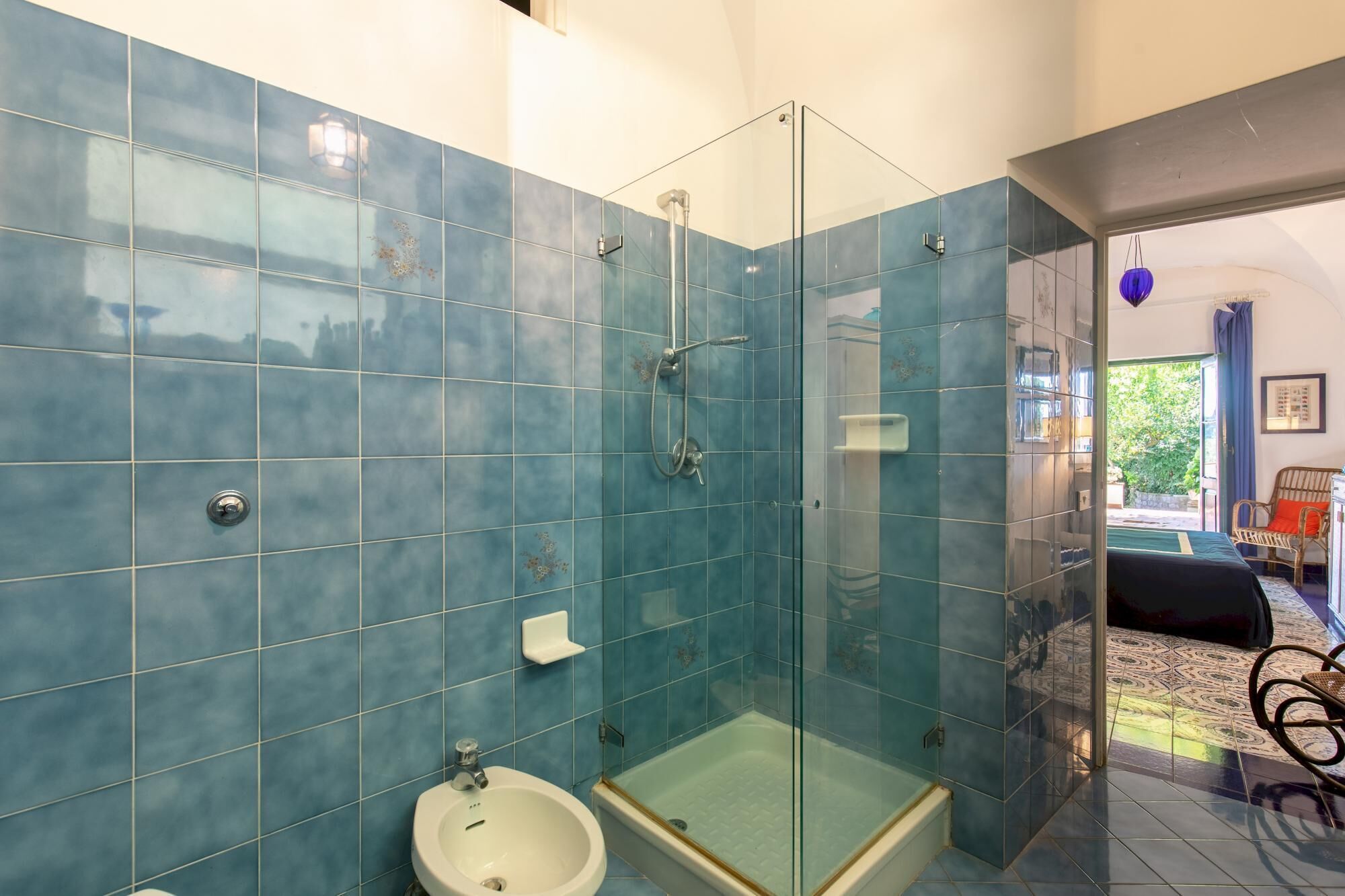 A bathroom with blue tiles, a glass shower enclosure, and a white sink.