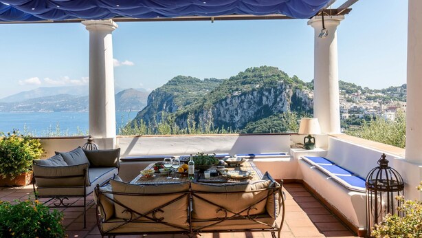 A terrace with a table set for dining, overlooking a mountainous landscape and the sea. - Villa Ginestra by Elite Villas (Capri)