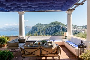 Une terrasse avec une table dressée pour le dîner, offrant une vue sur un paysage montagneux et la mer.