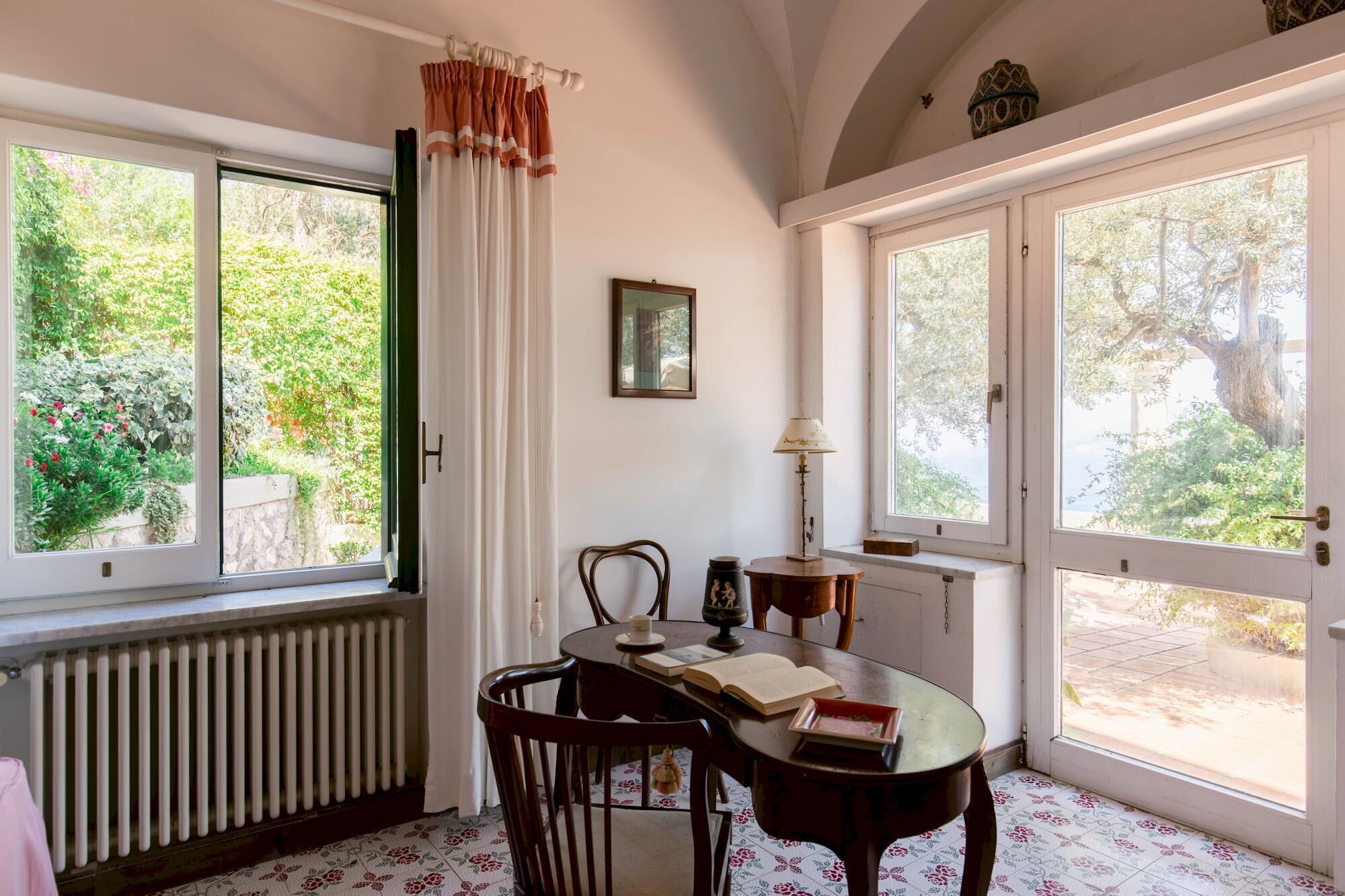 A room with a dining table, chairs, a radiator, and large windows with curtains.