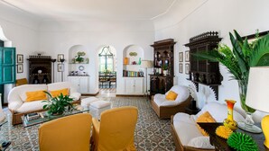 A spacious living room with a high ceiling, a dining area with a green archway, and a library with ornate wooden bookshelves. - Villa Ginestra by Elite Villas (Capri)