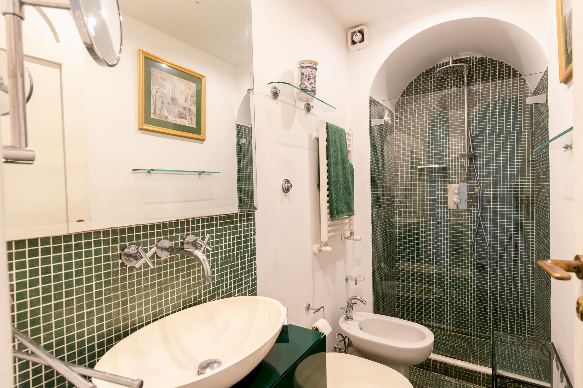 A bathroom with a large oval sink, a smaller sink, a glass shower enclosure, and a framed picture on the wall.