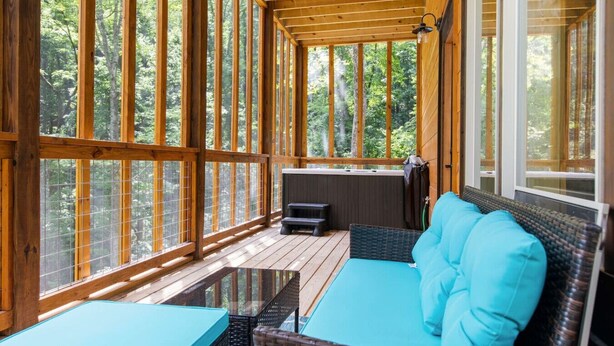 Een overdekt terras met een houten terras, een bank met blauwe kussens en een tafel.