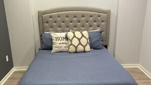 A bed with a tufted headboard, a blue bedspread, and two pillows with text. - One of a kind Luxury Loft (Dearborn)