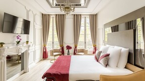 A spacious hotel room with a large bed, a TV, a desk, and a chandelier.