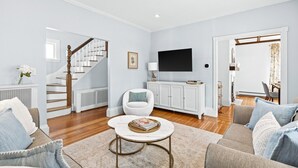 A living room with a staircase, a white sofa, a round coffee table, and a TV mounted on the wall. - 5 Bedroom Historic Home minutes to Boston with Yard (Medford)