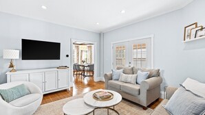 A living room with a sofa, coffee table, and TV. There is a dining area with a table and chairs. - 5 Bedroom Historic Home minutes to Boston with Yard (Medford)