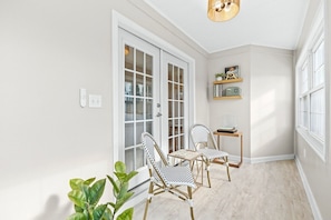 A room with a door, two chairs, a small table, a plant, and a shelf with books and a radio.