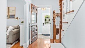 A hallway with a wooden floor, a white door, a staircase with white balusters, and a beige sofa. - 5 Bedroom Historic Home minutes to Boston with Yard (Medford)