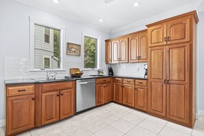 A kitchen with wooden cabinets, a dishwasher, and a window with a view of trees.