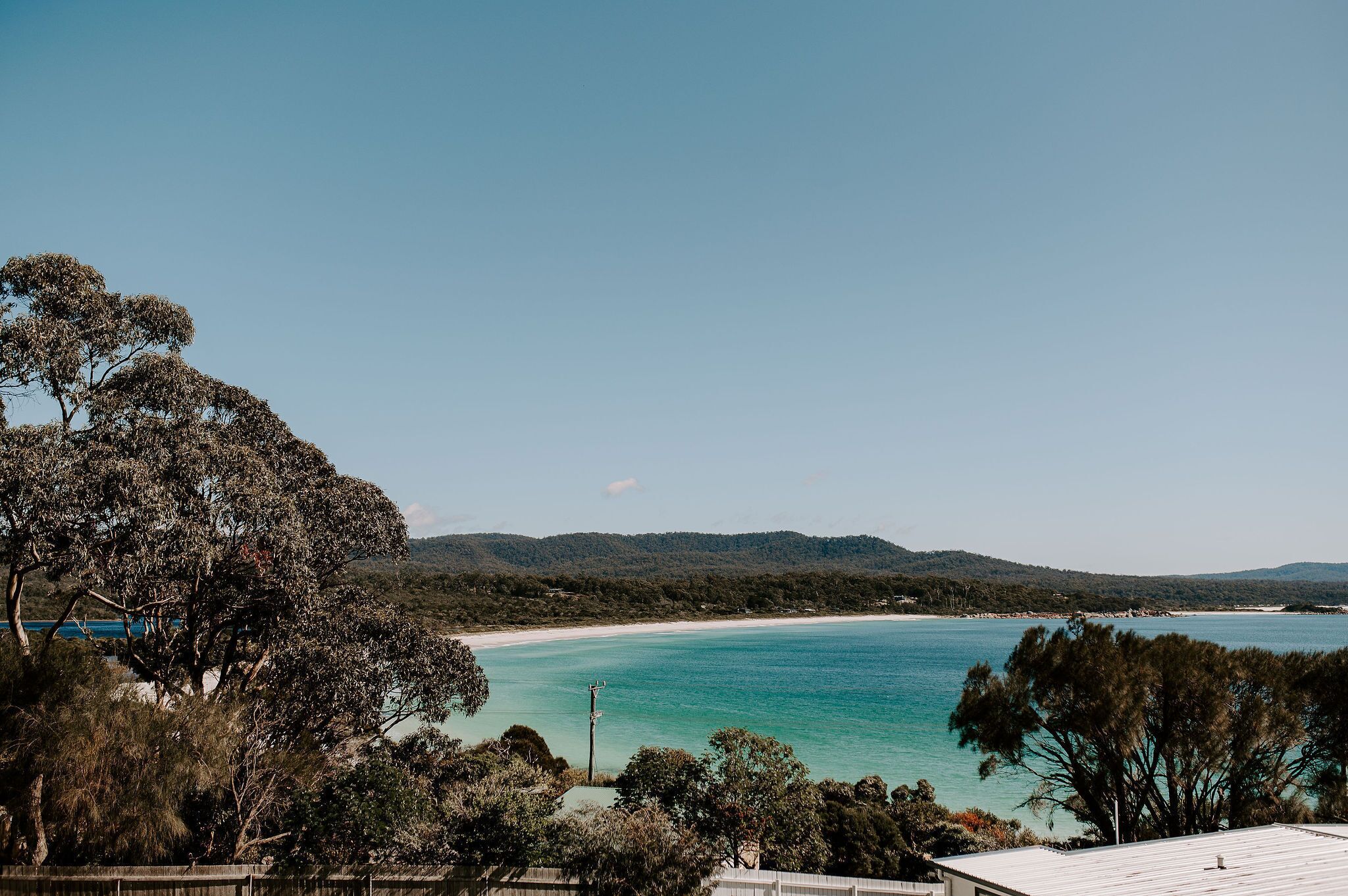 A coastal view with a beach, clear blue water, and a forested area.