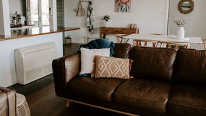 A cozy living room with a brown leather couch, a white coffee table, and a dining table with chairs. - THE BILLOWS - BINALONG BAY.  Hamptons style escape overlooking the Bay of Fires. (Binalong Bay)