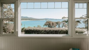 A room with a large window offering a view of a coastal landscape with trees and hills. - THE BILLOWS - BINALONG BAY.  Hamptons style escape overlooking the Bay of Fires. (Binalong Bay)