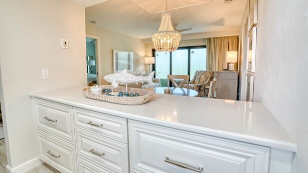 A hotel room with a large white vanity, a chandelier, and a view of the city through large windows. - Newly Renovated Park Shore Resort Deluxe Suite 238 (Naples)