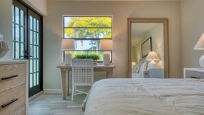 A bedroom with a bed, a desk with a chair, a window with a view of trees, and a mirror. - Newly Renovated Park Shore Resort Deluxe Suite 238 (Naples)