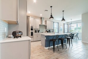 A modern kitchen with a central island, bar stools, and pendant lighting.