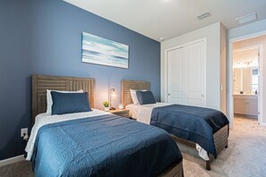 A bedroom with two beds, a nightstand with a lamp, a painting on the wall, and a door leading to a bathroom.