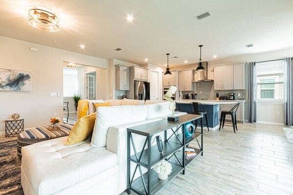 A modern living room with a sofa, a coffee table, and a kitchen area with a dining table and bar stools.