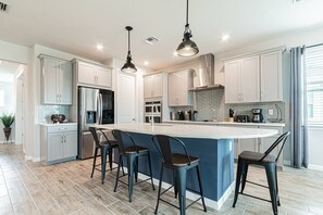 A modern kitchen with a large island, stainless steel appliances, and pendant lighting.