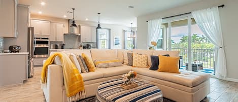 A modern living room with a sectional sofa, ottoman, and a view of the outdoors through large windows.