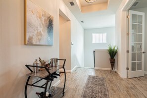 A hallway with a dining area featuring a metal table and chairs, a large abstract painting, and a potted plant.