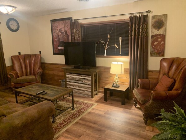 A living room with a television, two leather armchairs, a coffee table, and a lamp.