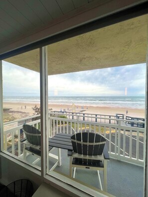 Ein Balkon mit zwei Stühlen und einem Tisch, der Blick auf einen Strand mit einem entfernten Turm bietet.