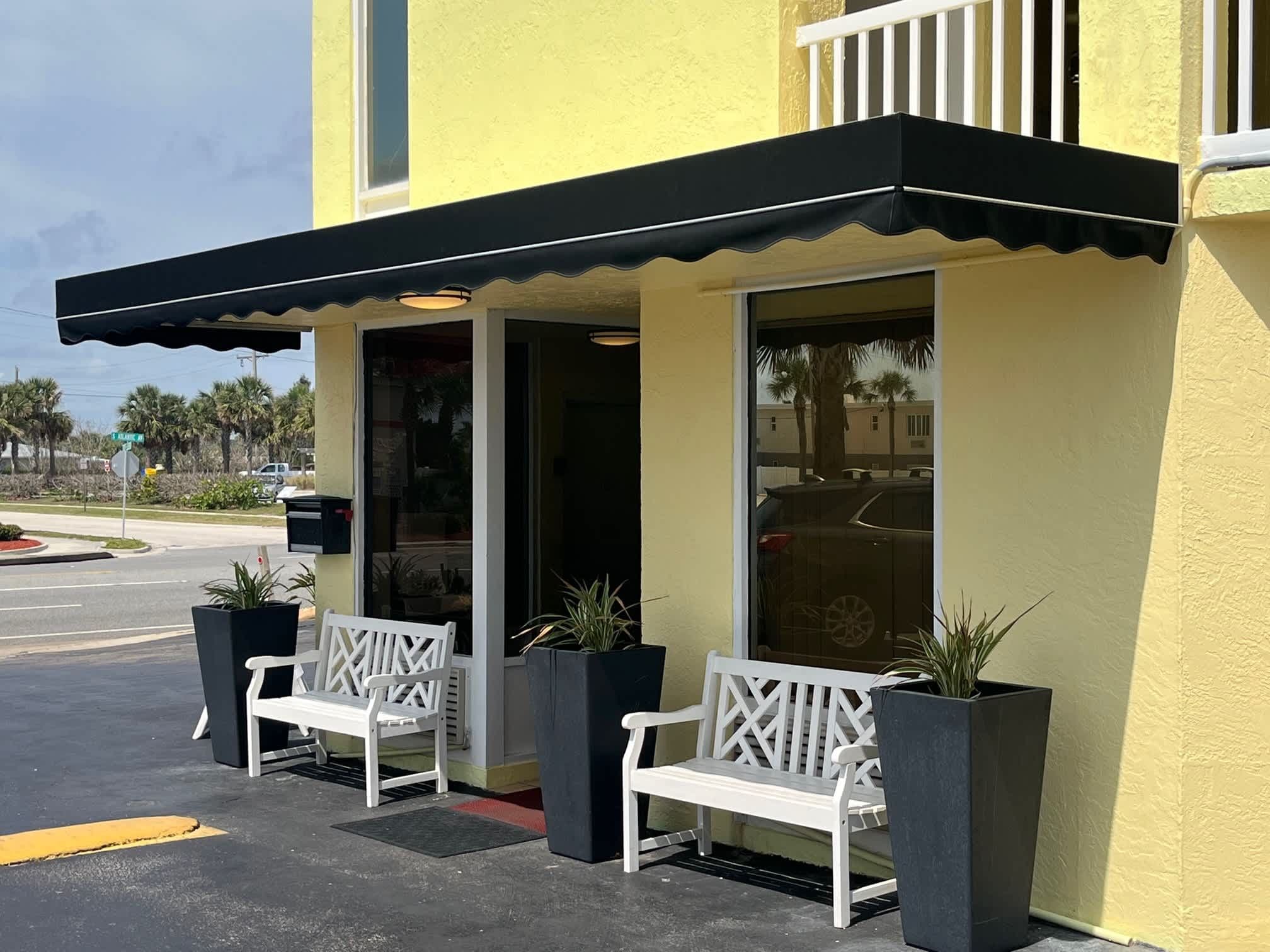 A building with a yellow exterior, a black awning, and two white benches outside.