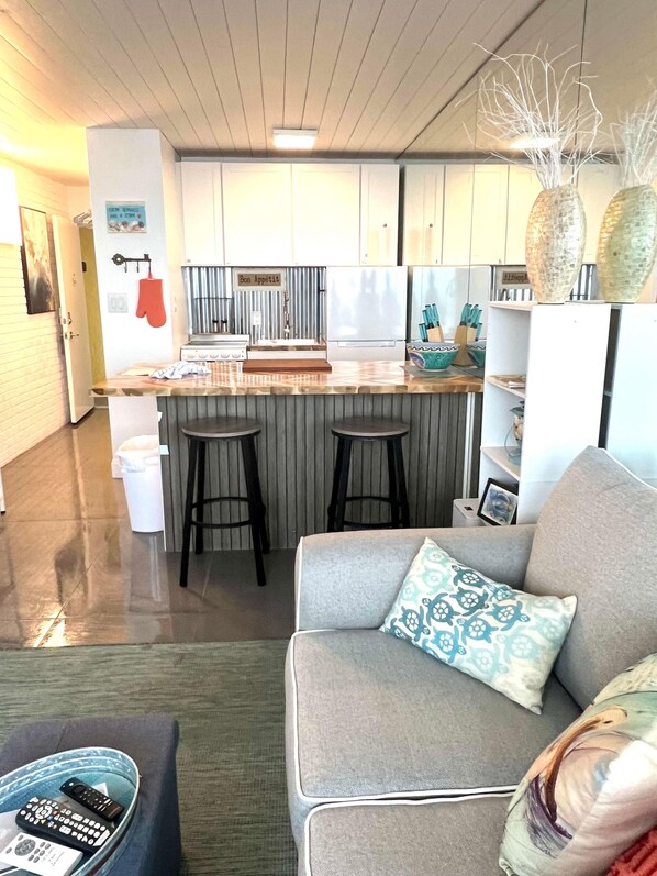 Eine moderne Küche mit Kochinsel, Barhocker und Essbereich inklusive Sofa und Fernbedienungen.
