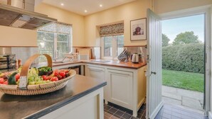 Una cocina con frutero, armarios blancos, una ventana y una puerta que da a un jardín.