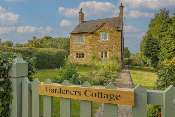 Una cabaña de piedra con un letrero que dice 'Gardeners Cottage' en la entrada.