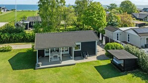 A modern residential area with a house featuring a patio with outdoor furniture, surrounded by lush greenery and a view of the sea. - "Iven" - 140m from the sea by Interhome (Otterup)