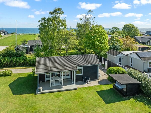 Un quartier résidentiel moderne avec une maison dotée d’un patio aménagé avec du mobilier d’extérieur, entouré d’une végétation luxuriante et offrant une vue sur la mer.