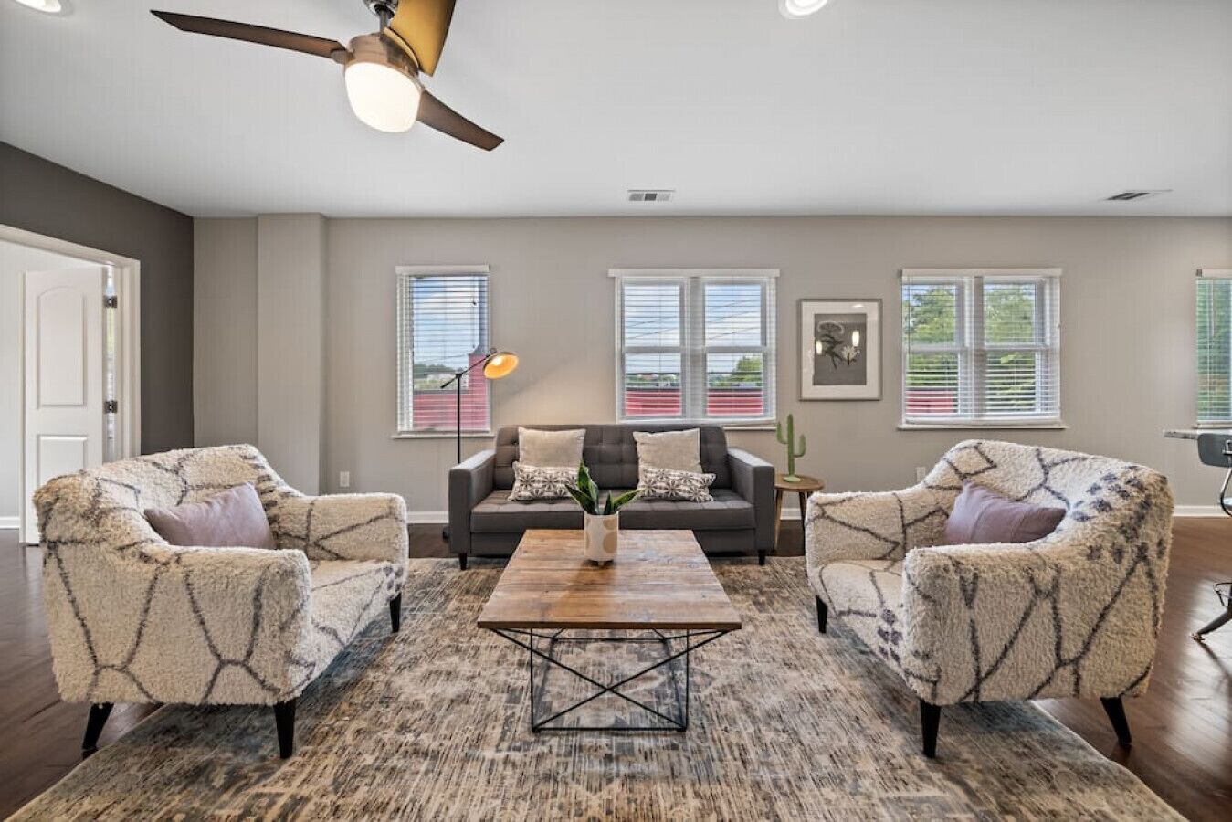 A living room with a sofa, two armchairs, a coffee table, and a ceiling fan.