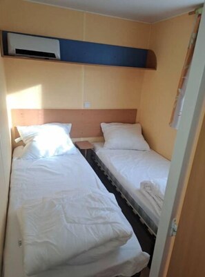 Een kleine, praktische kamer met twee eenpersoonsbedden, een houten hoofdbord en een wandairconditioner.