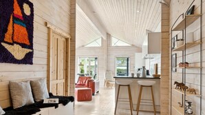 Un interior moderno con paredes de madera, un rincón de descanso acogedor, una cocina con taburetes de bar y vistas a través de un ventanal grande.