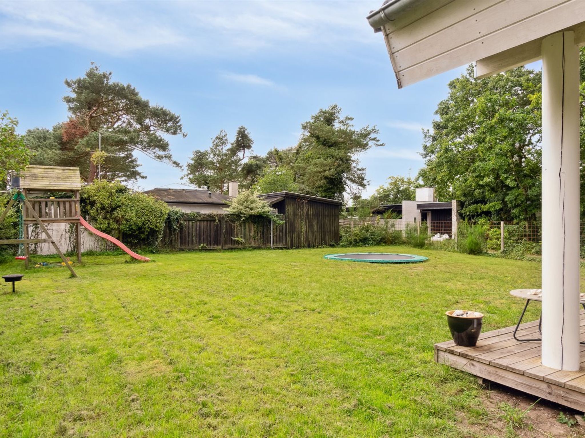 Un patio trasero con un parque infantil de madera, un trampolín y un cobertizo.