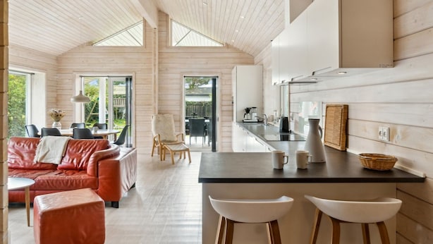 Un interior moderno con techo de madera, una zona de cocina, un comedor con sofá de cuero rojo y una barra con taburetes.