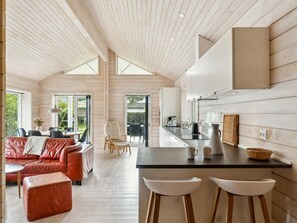 Un interior moderno con techo de madera, una zona de cocina, un comedor con sofá de cuero rojo y una barra con taburetes.