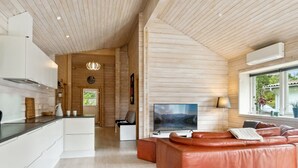 Una sala de estar moderna con un sofá de cuero, un televisor de pantalla plana y un amplio ventanal con vistas al exterior.