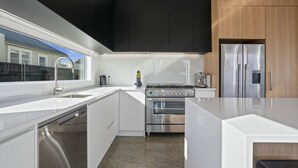 A modern kitchen with white cabinetry, a stainless steel refrigerator, a built-in oven, and a window providing a view of the outside. - Stylish Serenity - Martinborough Holiday Home (Martinborough)