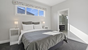 A modern bedroom with a large bed, two bedside tables, a window with a view, and a walk-in closet. - Stylish Serenity - Martinborough Holiday Home (Martinborough)