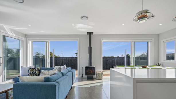 A modern kitchen with a central island, a built-in stove, and large windows offering views of the backyard. - Stylish Serenity - Martinborough Holiday Home (Martinborough)