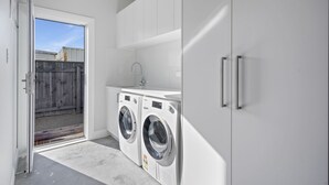 A laundry room with two front-loading washing machines, a sink, and a door leading to an outdoor area. - Stylish Serenity - Martinborough Holiday Home (Martinborough)